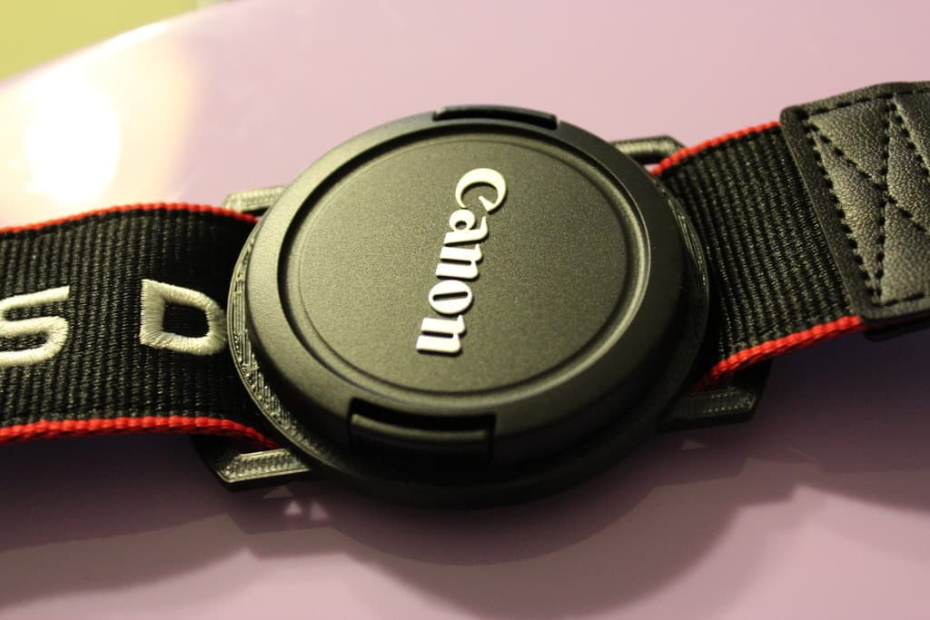 Camera lens cap holder buckle on a strap